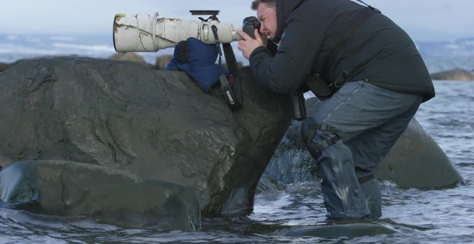 A man is using a camera with a large lens in the water