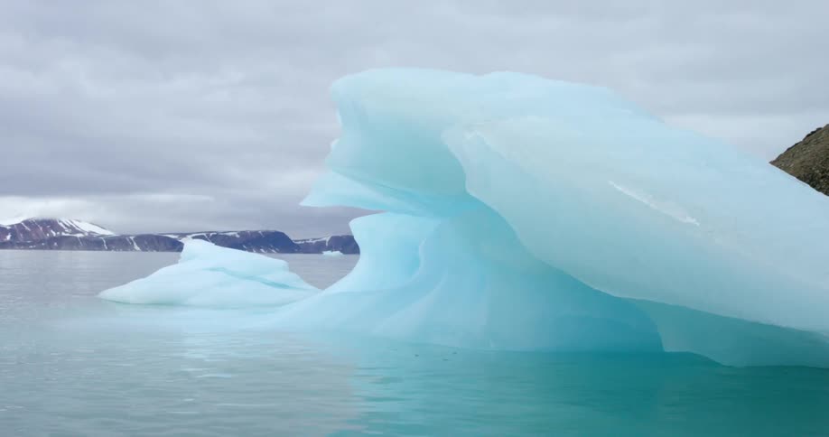 An iceberg floating in the sea under a heavily clouded winter sky