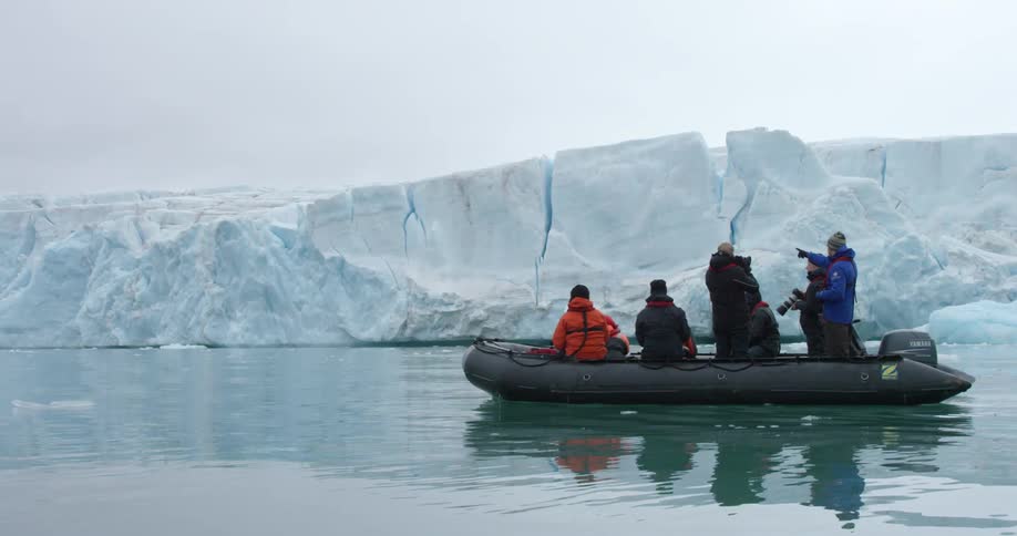 A group of people in a rubber boat are stopped looking at the edge of a glacier