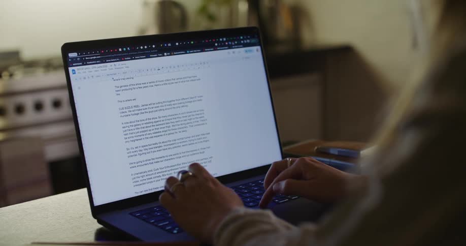 A woman is sitting at a table typing on a laptop computer keyboard