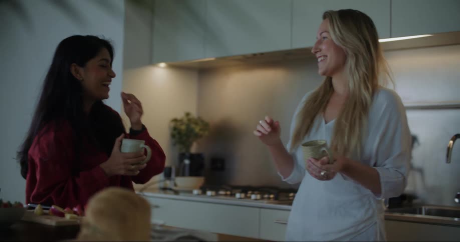 Two friends eating breakfast together talk and laugh in the kitchen at home