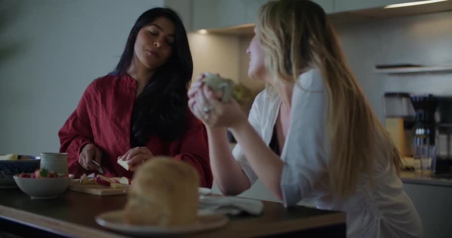 Two friends making breakfast together talk and laugh in the kitchen at home