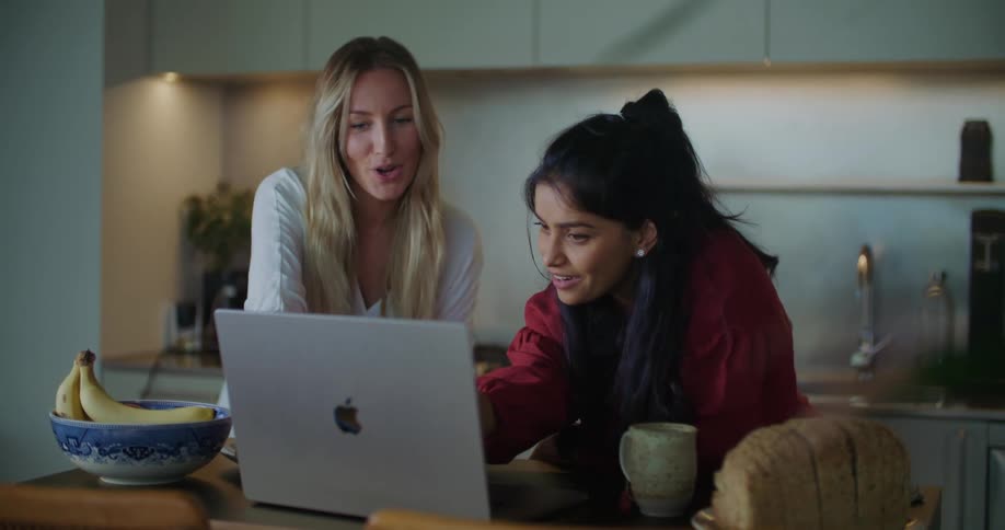Two women are looking at a laptop computer and laughing