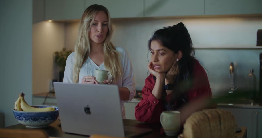 Women discuss contents of laptop set on table near the kitchen