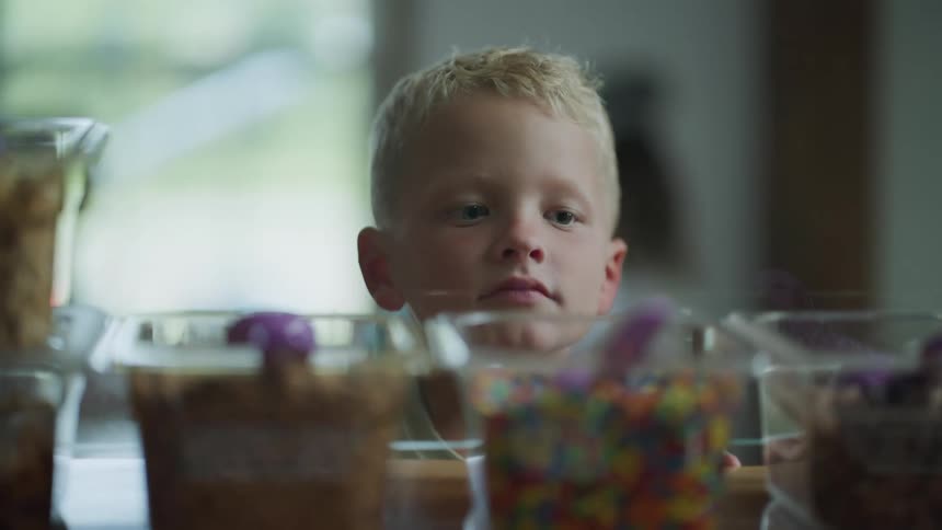 A young boy is looking at containers of ice cream toppings on the counter top in a shop