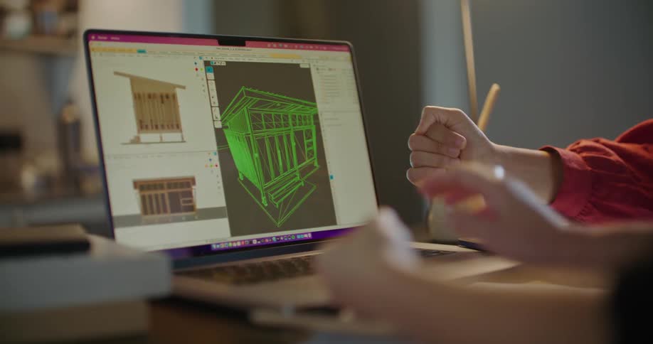 Two women sit at desk in an office and look at drawings on a laptop