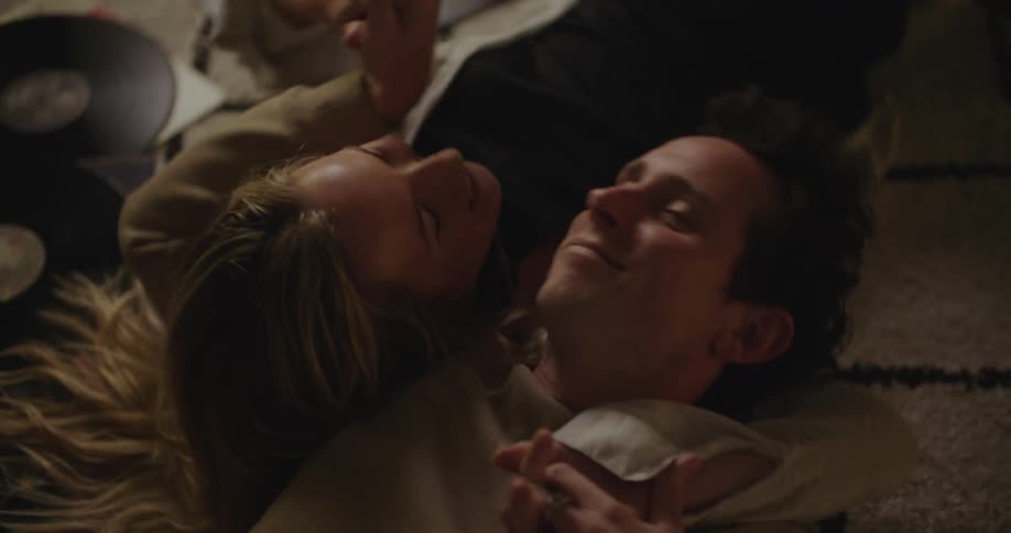 A man kisses a woman on the cheek while laying on the floor and holding hands