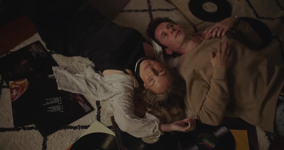 A man and a woman have a conversation while laying on the floor near vinyl records