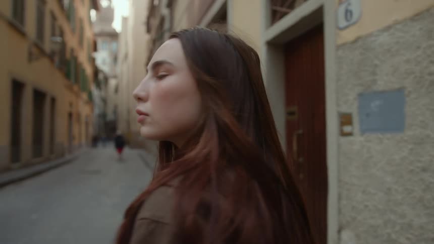 A woman looks up at buildings while walking down a city alley