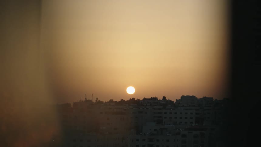 The sun is set low in the sky above a city thats densely packed with buidlings