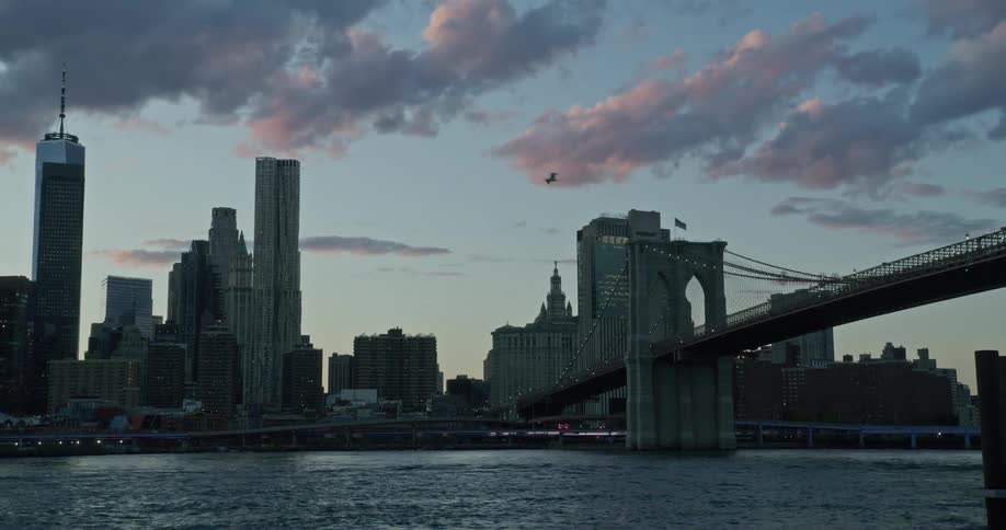 A view of a city skyline at dusk with a bridge over a waterway and skyscrapers behind it