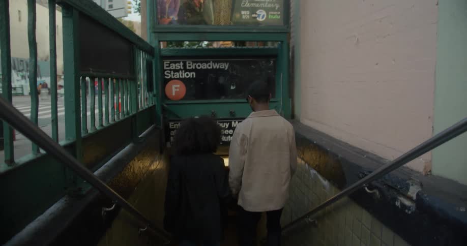 Couple walks down staircase to subway as vehicles move along downtown street