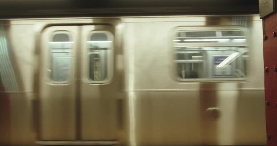 A shiny silver subway train slows as it pulls into a subway station