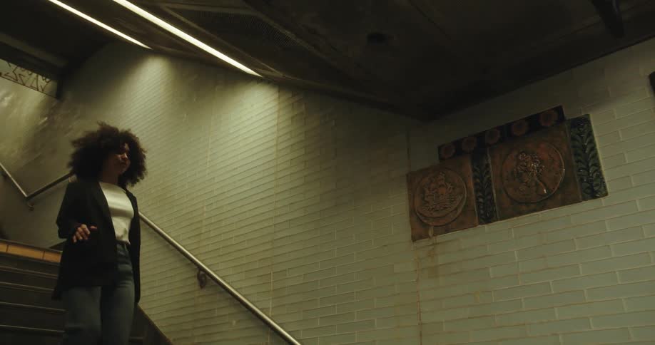Young woman with a big bouncy afro walks down the stairs on the subway