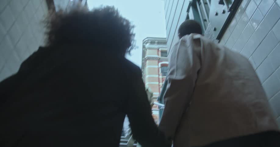 Couple holding hands climb a staircase out of a metro station in the city