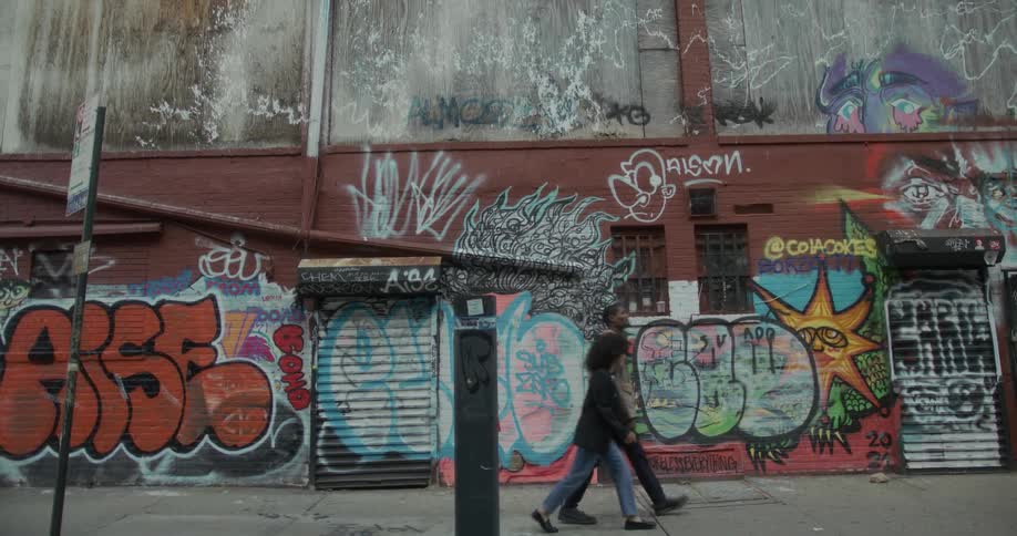 A man and woman walk down an urban city street before a wall covered in colorful graffiti art