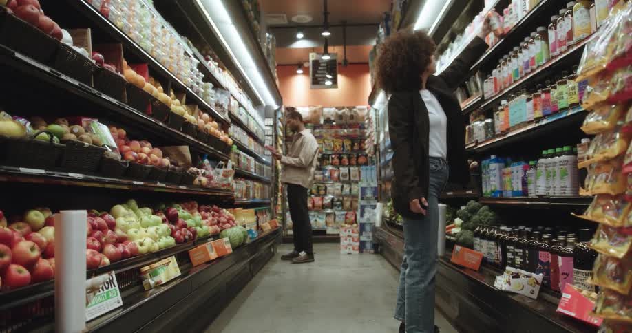 Grocery store aisle with produce and beverages a man and a woman separately inspecting items on the selves