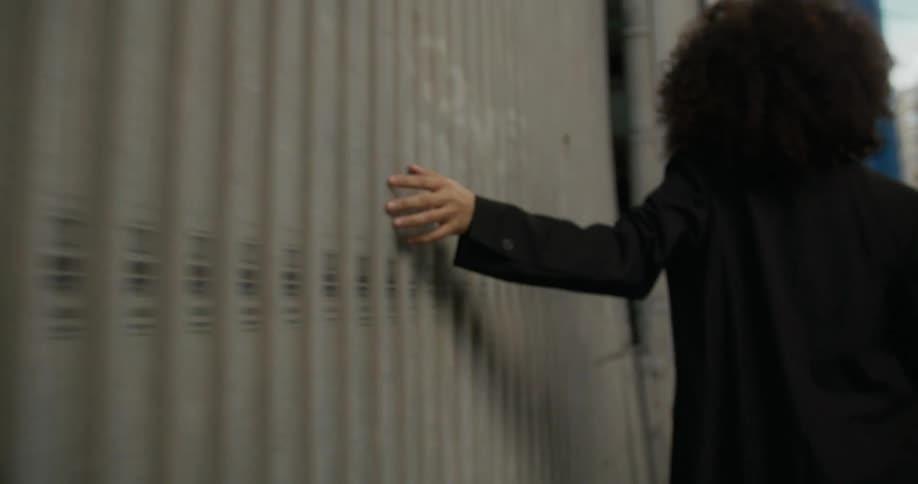 Person moves along side of building running hand on wall
