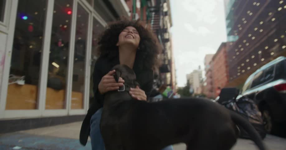 Young girl crouch on the city street to greet a happy black pet dog