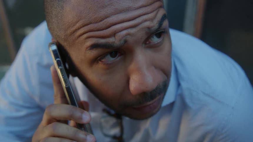 A man is sitting outdoors and talking on the phone