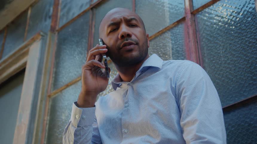 A man in a blue dress shirt carries on a conversation on his cell phone