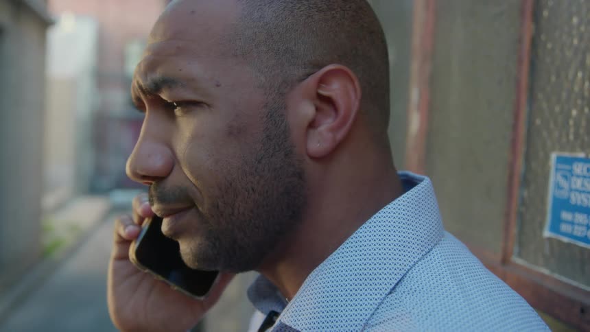 Man with stubble beard and shirt talks on mobile phone in the narrow street