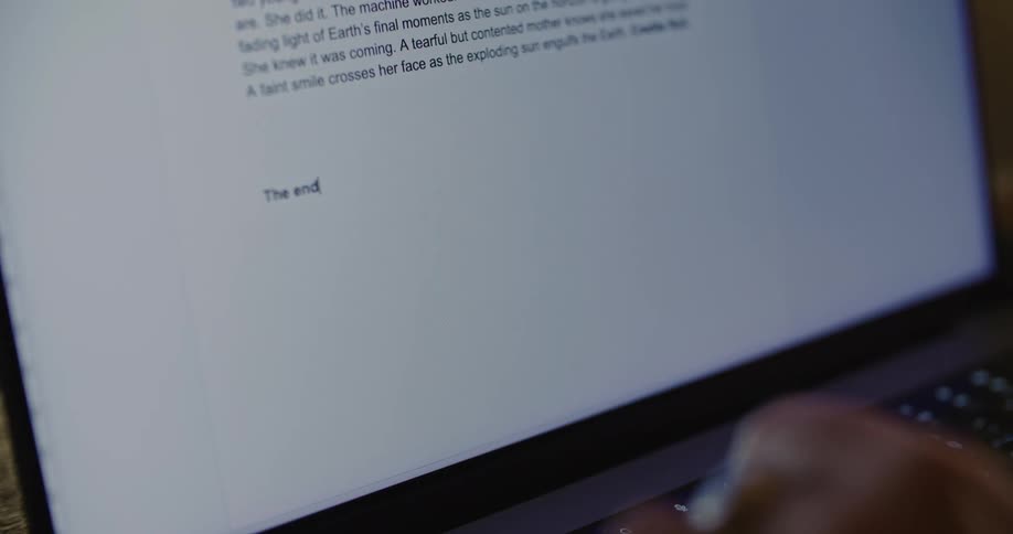 A persons hand is seen typing a story on a laptop computer
