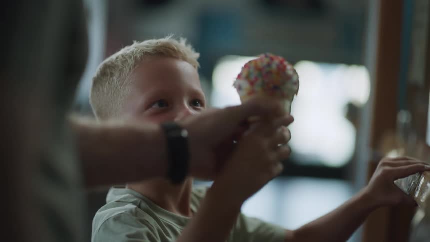 A father hands an excited boy a sprinklecovered cone at an ice cream parlor