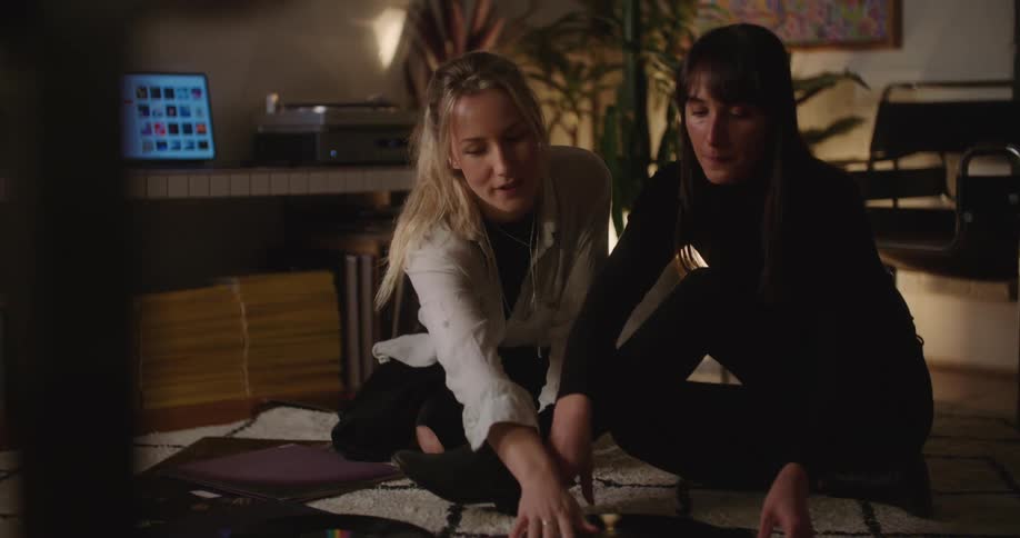 Two women sit on the floor indoors and look at album covers