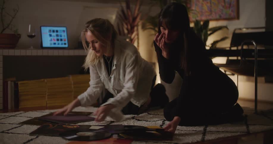 Two women knelt down on a carpet going through albums and records