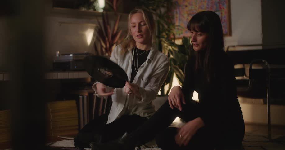 Two women are sitting on a rug on the floor looking at a vinyl record album