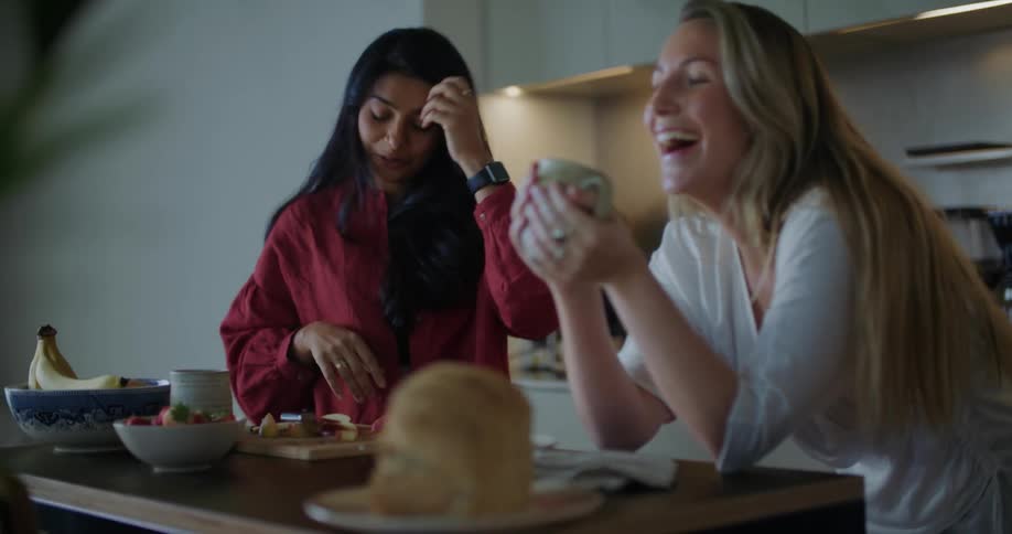 Two friends eating breakfast together talk and laugh in the kitchen at home