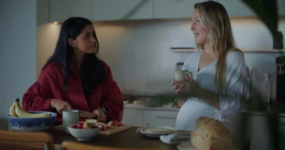 Two women standing in a kitchen talking and laughing while one is cutting up food