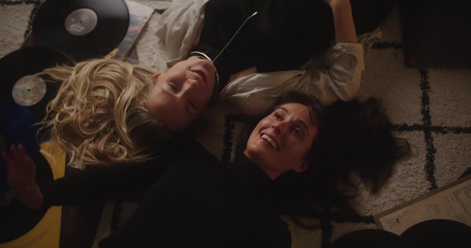 Two women lay on the floor near record albums looking up at the ceiling