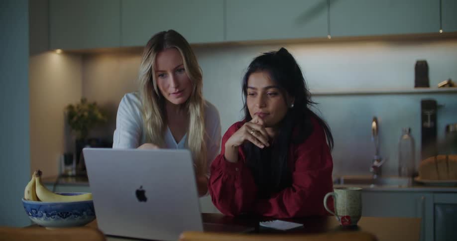 Two women talk while looking at a laptop