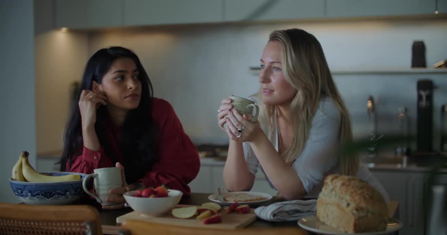 Two women sitting at a kitchen table chatting over coffee and breakfast