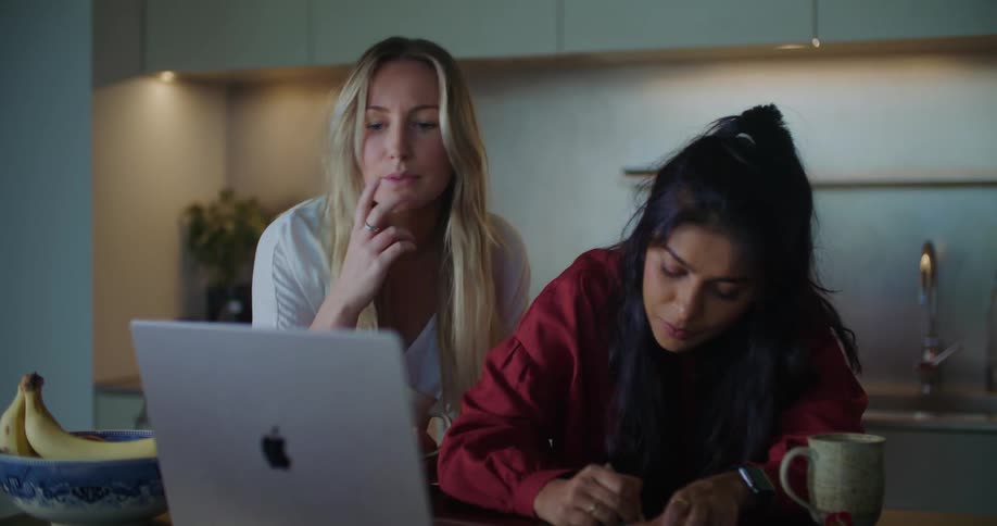 Two friends reading on a laptop screen take notes in the kitchen at home