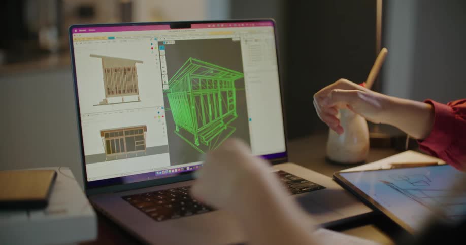 Two people point at blueprints on the laptop