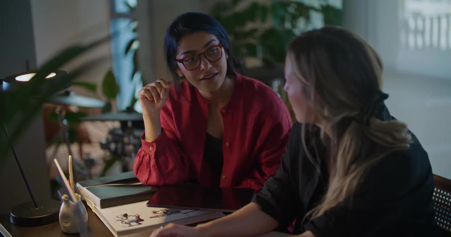 Two female coworkers talk while sitting a at a desk in an office