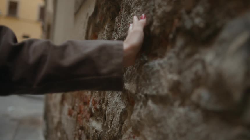 A woman is gliding her hand against a bumpy rock wall