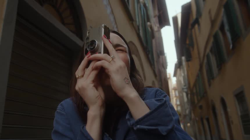 Close up of a young woman taking pictures with a camera while walking on a narrow european alley