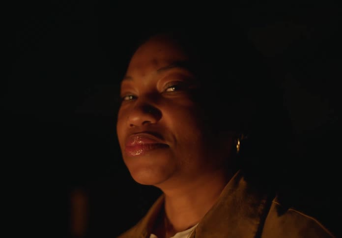 Woman with earrings and brown jacket smiles at camera next to bonfire at night
