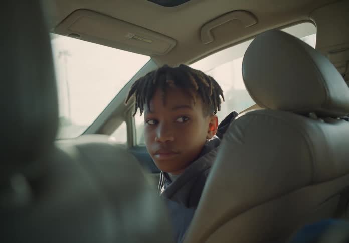 A young boy is sitting in the passenger seat of an automobile and he turns his head to look in the back seat
