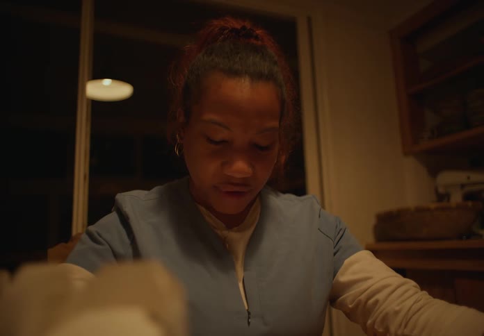 A black woman takes a deep breath while speaking as she sits indoors