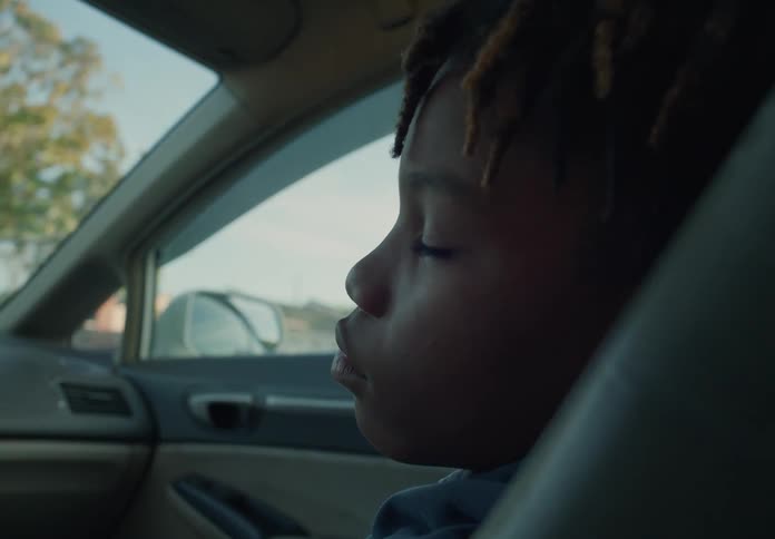 A little boy is sleeping in the passenger seat of an automobile traveling through a neighborhood