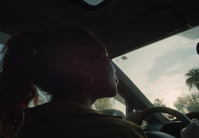 Bright sunlight shines on a womans face as she drives her automobile through a neighborhood