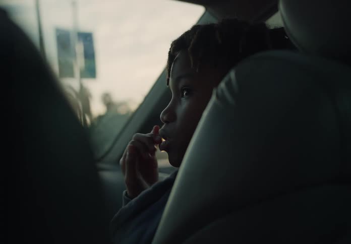 A boy sits in the passenger seat of a car and looks over to the driver and smiles