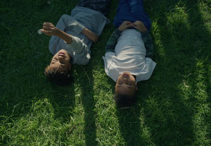 Two boys chat while lying on the grass
