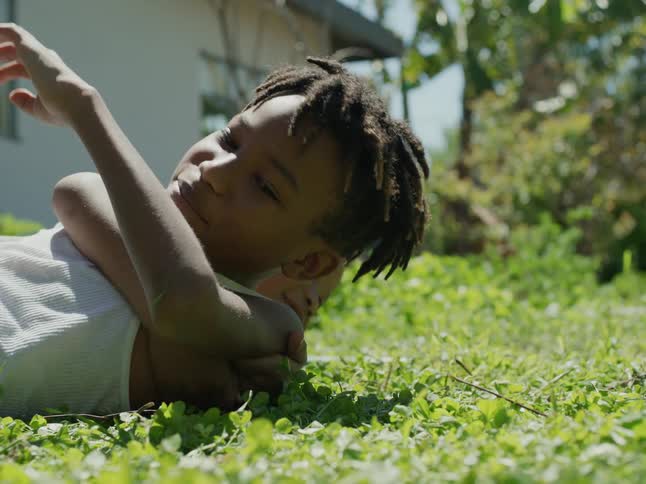 A boy is laying in the grass when another boy playfully jumps on him