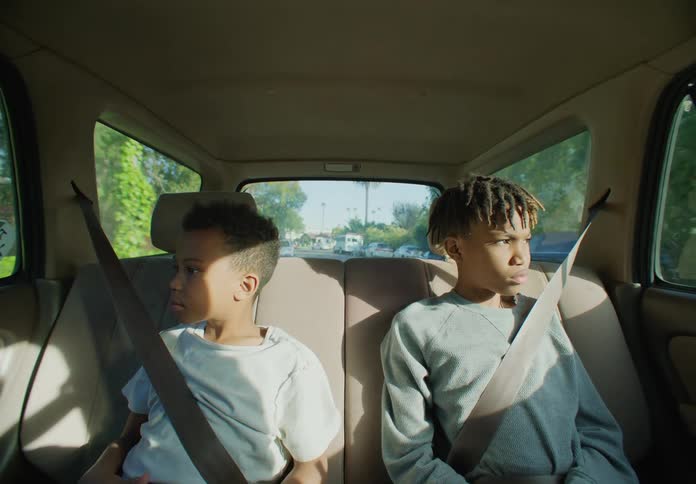 Two boys are sitting in the back seat of a traveling automobile with their seat belts on